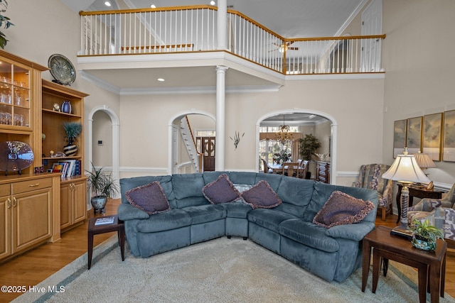 living room featuring crown molding, arched walkways, a high ceiling, and an inviting chandelier
