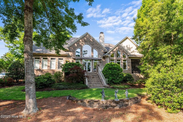 view of front of home featuring a chimney, a front lawn, and brick siding