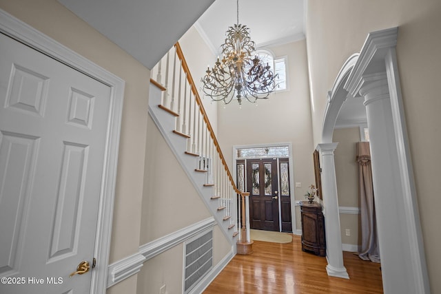 foyer entrance with visible vents, crown molding, stairs, wood finished floors, and a notable chandelier
