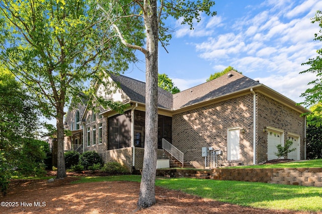 rear view of property with roof with shingles, brick siding, a garage, a sunroom, and a yard