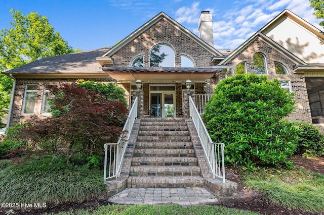 view of front of house with a porch, brick siding, a chimney, and stairs