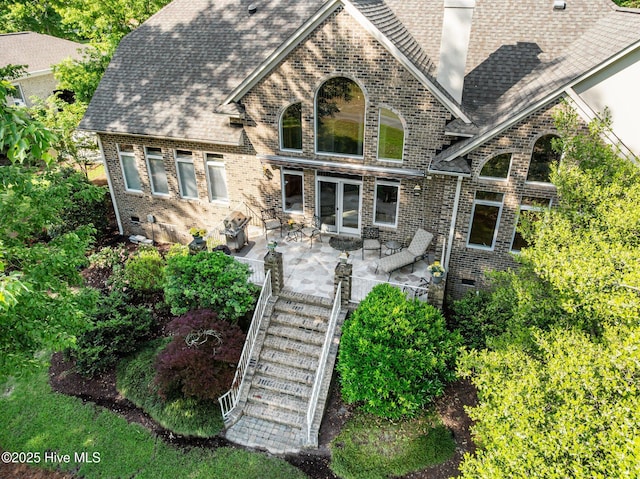 exterior space with brick siding, a shingled roof, and a patio area