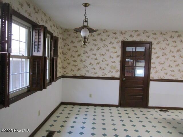 unfurnished dining area featuring baseboards, wallpapered walls, and light floors