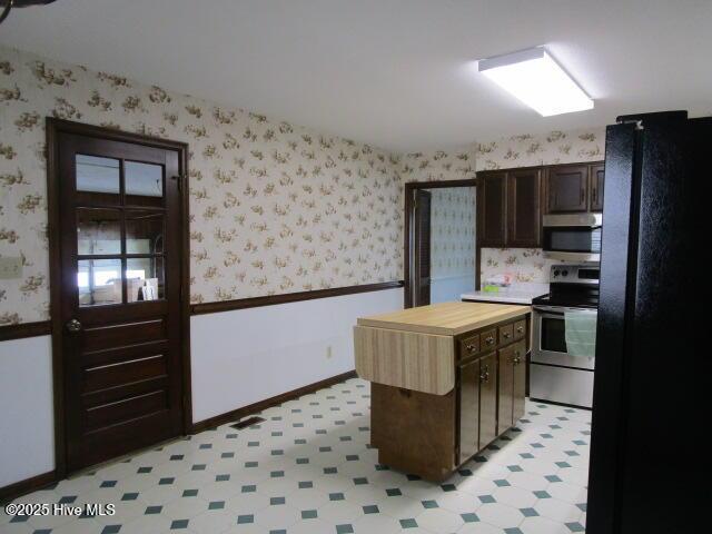 kitchen with dark brown cabinetry, light floors, butcher block counters, appliances with stainless steel finishes, and wallpapered walls