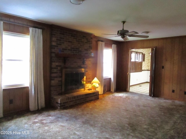 unfurnished living room with wooden walls, a fireplace, a ceiling fan, and carpet floors