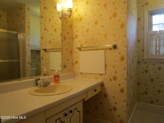 full bath with wallpapered walls, toilet, a stall shower, and vanity