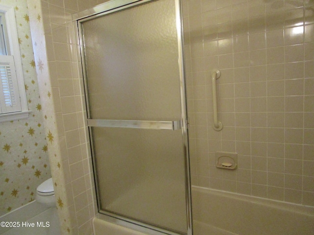 bathroom featuring toilet, wallpapered walls, and a shower with door