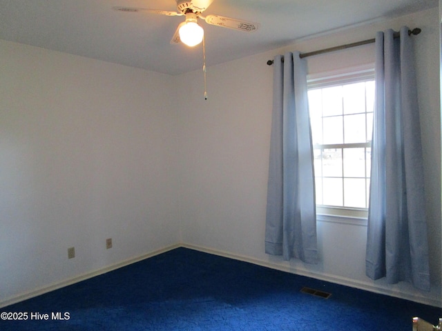 carpeted spare room featuring a wealth of natural light, visible vents, baseboards, and ceiling fan