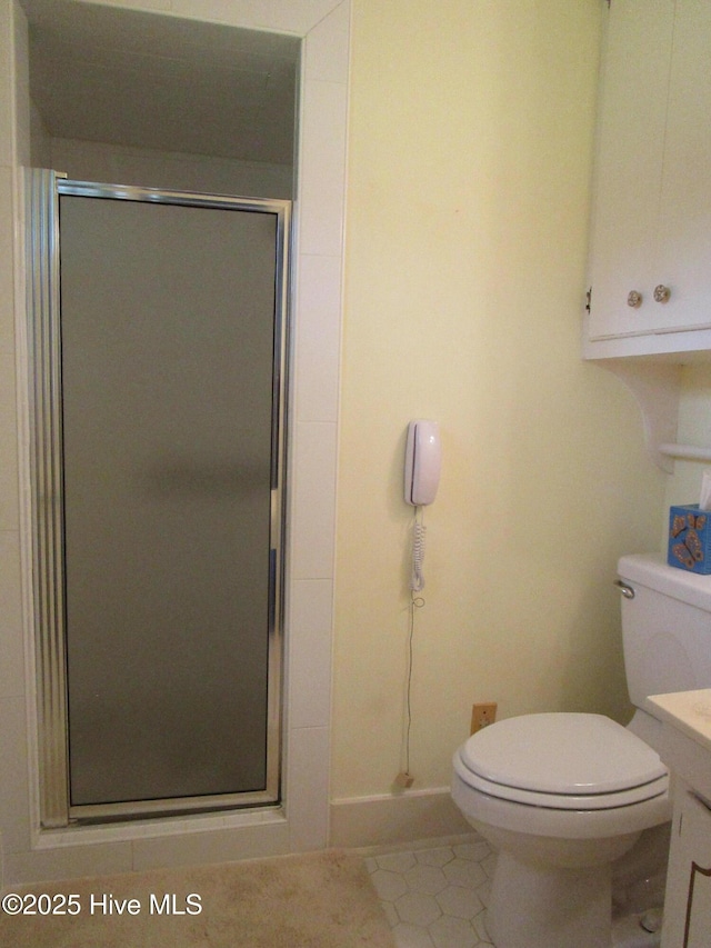 bathroom with baseboards, toilet, vanity, tile patterned flooring, and a stall shower