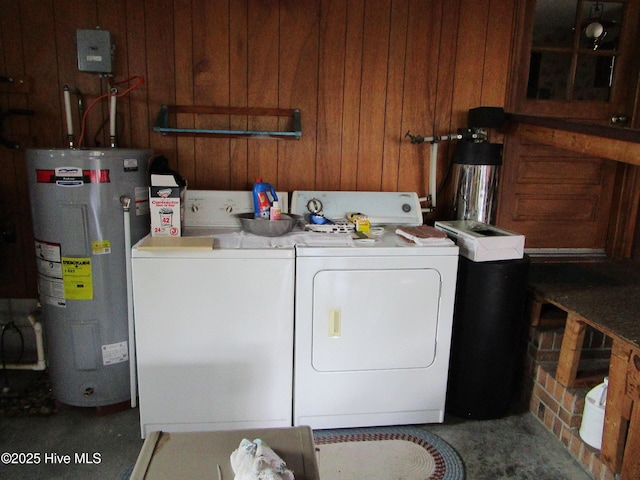 clothes washing area featuring electric water heater, wood walls, separate washer and dryer, and laundry area