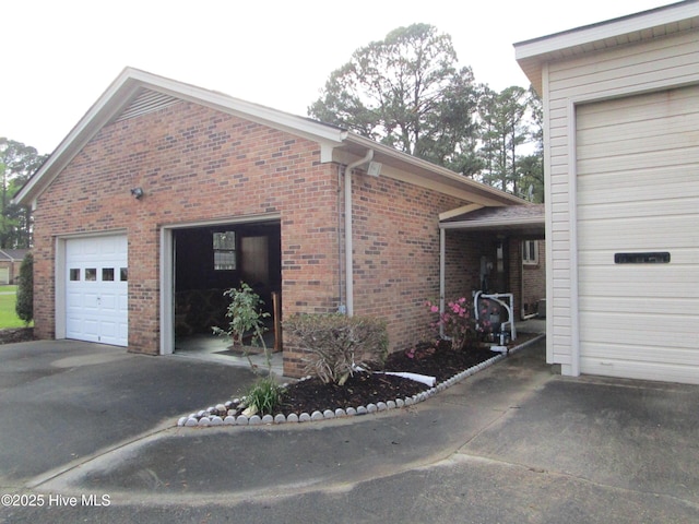 view of side of property featuring brick siding, a garage, and aphalt driveway