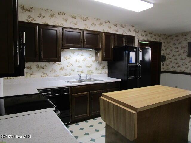 kitchen with light floors, black appliances, a sink, butcher block countertops, and wallpapered walls
