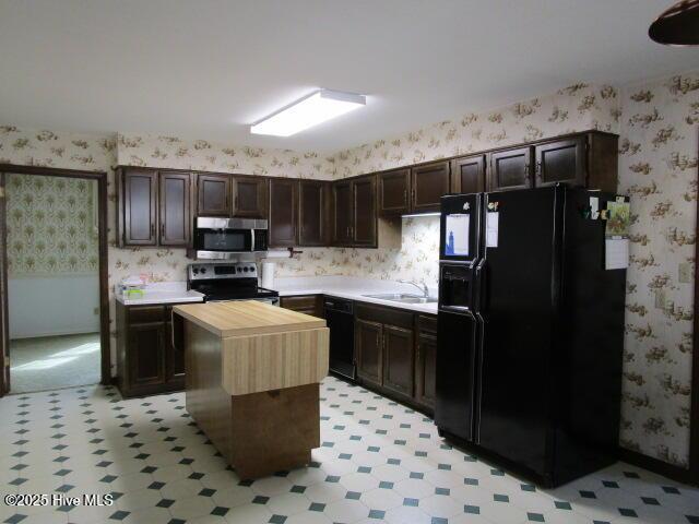 kitchen with wooden counters, wallpapered walls, black appliances, and light floors
