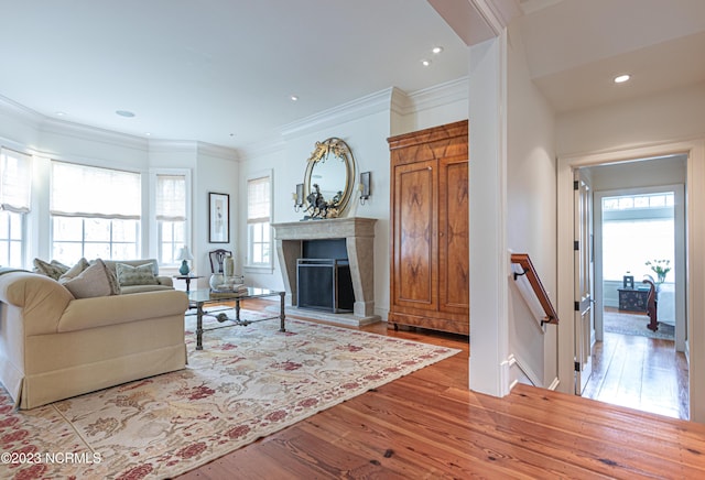 living area featuring recessed lighting, a fireplace with raised hearth, ornamental molding, and wood finished floors