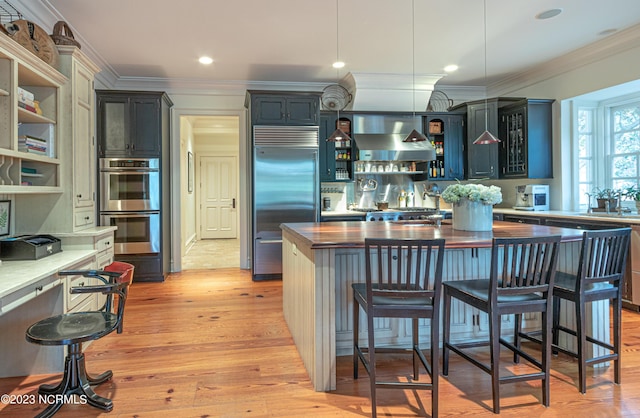 kitchen featuring ornamental molding, wall chimney range hood, open shelves, light wood-style floors, and appliances with stainless steel finishes