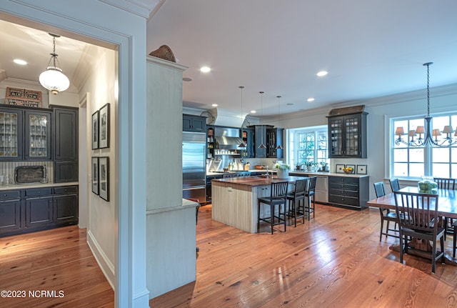 kitchen with butcher block counters, light wood-type flooring, built in fridge, and ornamental molding