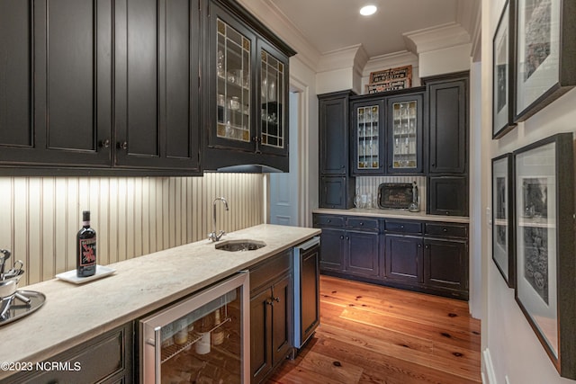 bar with light wood-style floors, ornamental molding, stainless steel microwave, a sink, and beverage cooler
