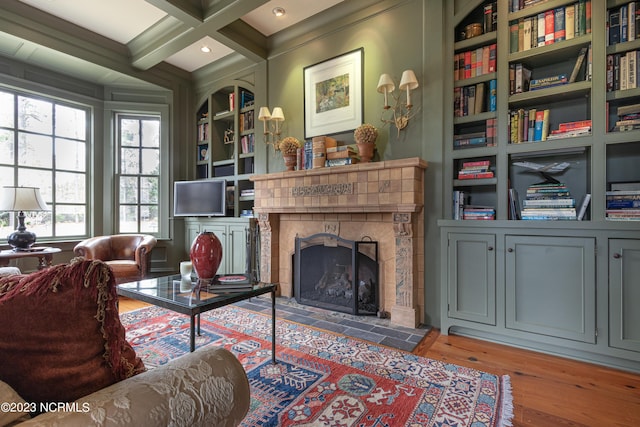living area featuring built in shelves, beamed ceiling, wood finished floors, coffered ceiling, and a tile fireplace