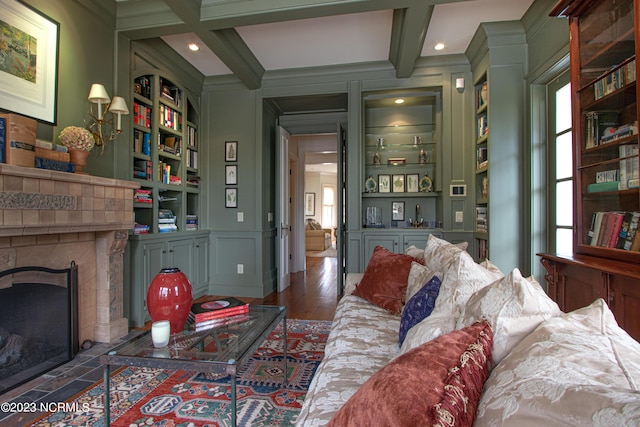 living area with built in features, ornamental molding, beamed ceiling, coffered ceiling, and a tile fireplace