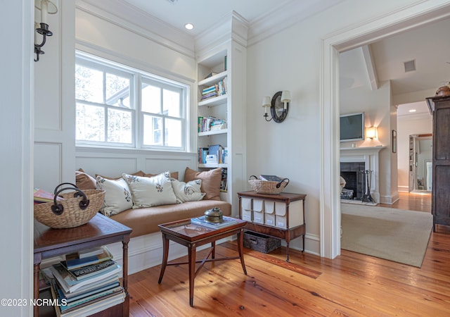 living area featuring built in features, visible vents, ornamental molding, a fireplace, and light wood finished floors