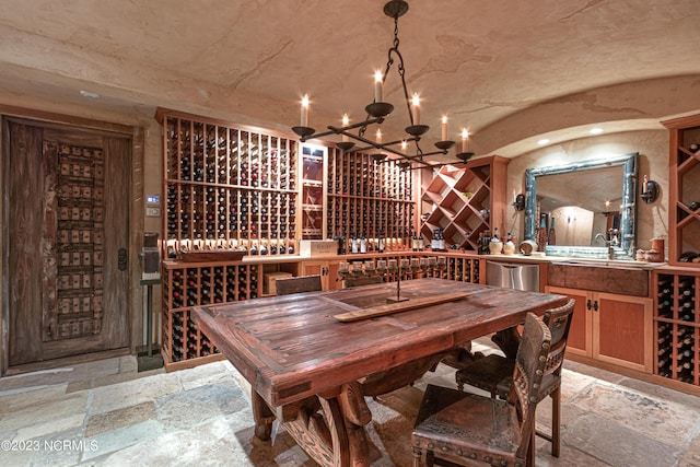 wine room featuring a sink, stone tile flooring, a chandelier, and vaulted ceiling