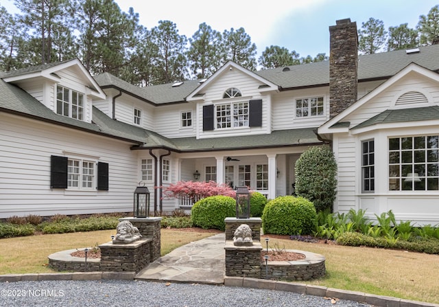 view of front facade with a chimney, a shingled roof, and ceiling fan