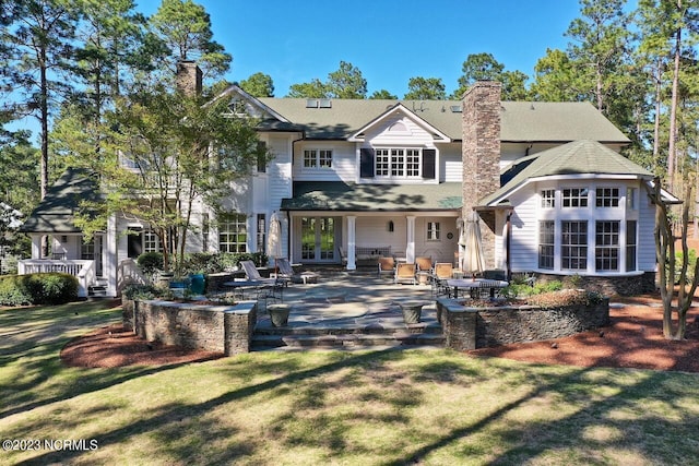 rear view of property featuring french doors, a patio, a lawn, and a chimney
