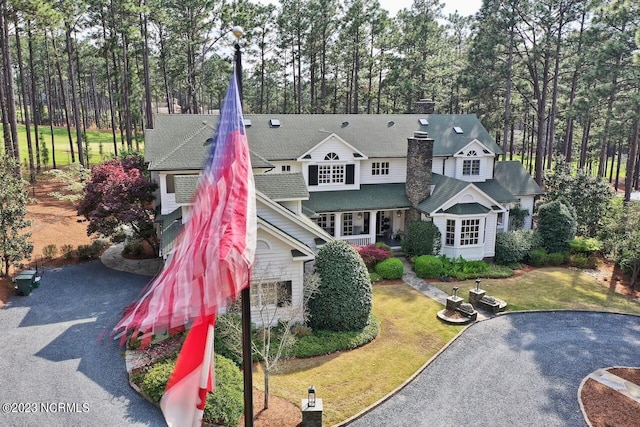 view of front facade with a front yard, a shingled roof, and a chimney