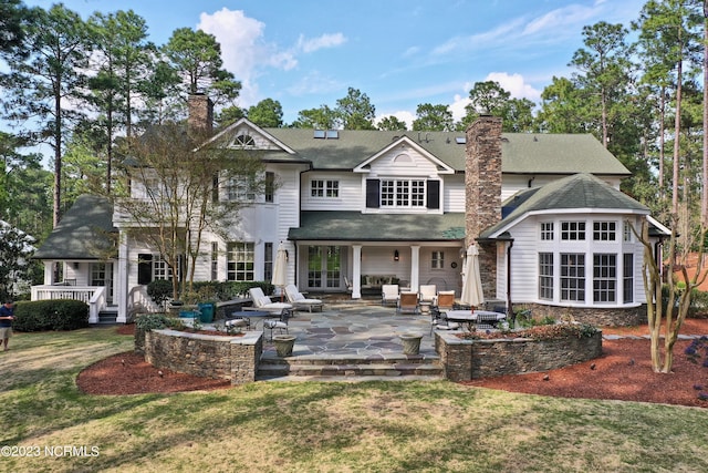 rear view of property with a patio area, roof with shingles, a lawn, and a chimney