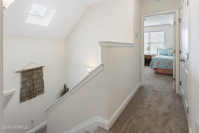 corridor with carpet flooring, an upstairs landing, baseboards, and vaulted ceiling with skylight