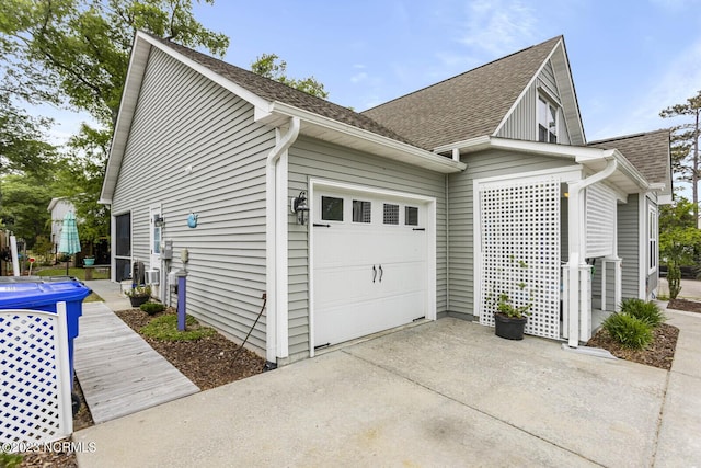 view of side of home featuring an attached garage, roof with shingles, and driveway