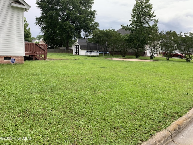 view of yard with a shed, a trampoline, a deck, and an outbuilding