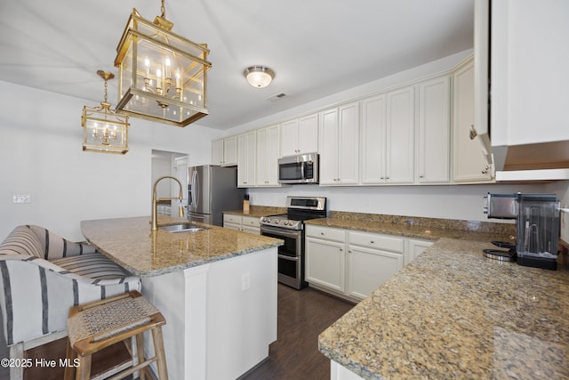 kitchen featuring visible vents, a sink, dark wood-type flooring, stainless steel appliances, and an island with sink