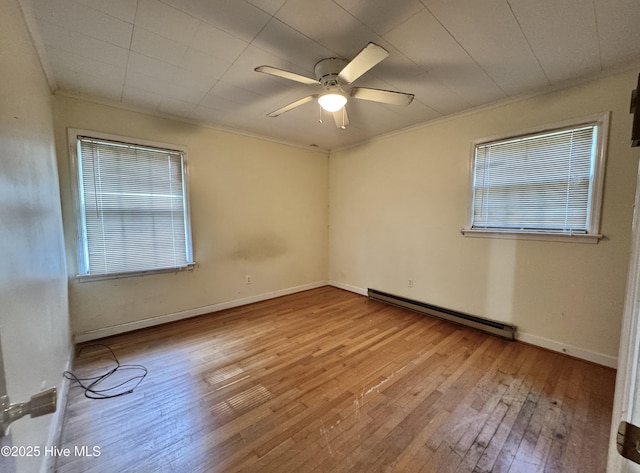 spare room featuring a ceiling fan, a baseboard heating unit, a healthy amount of sunlight, and hardwood / wood-style floors