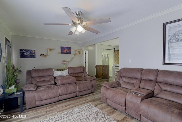 living area with ornamental molding, light wood-style flooring, a ceiling fan, and a barn door