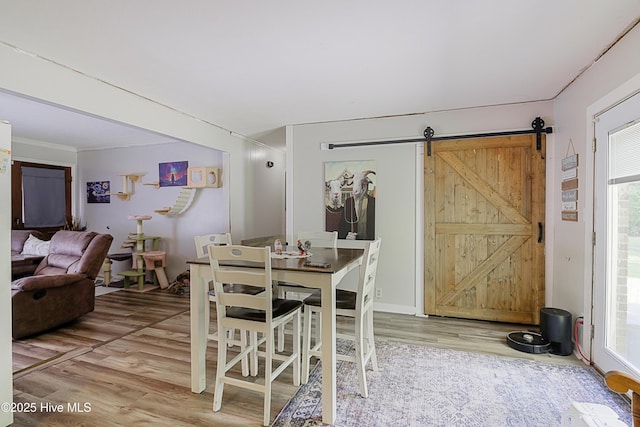 dining space with crown molding, wood finished floors, a barn door, and a healthy amount of sunlight