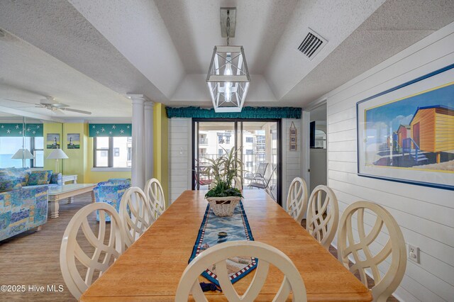 dining area featuring visible vents, decorative columns, wooden walls, a textured ceiling, and a ceiling fan
