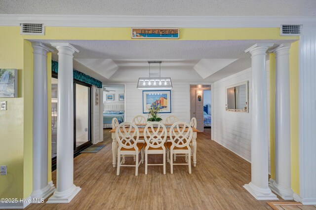 dining room with a textured ceiling, decorative columns, wood finished floors, and visible vents