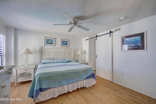 bedroom with ceiling fan, a barn door, light wood finished floors, a textured ceiling, and visible vents