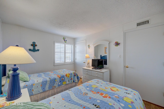 bedroom with visible vents, a textured ceiling, and wood finished floors
