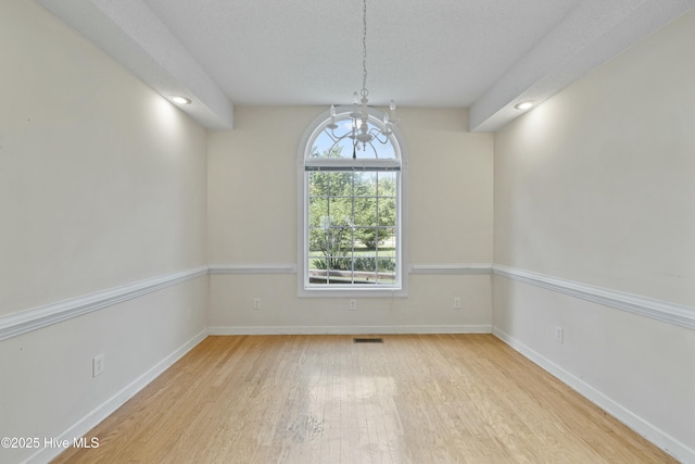 unfurnished dining area with wood finished floors, an inviting chandelier, baseboards, and visible vents