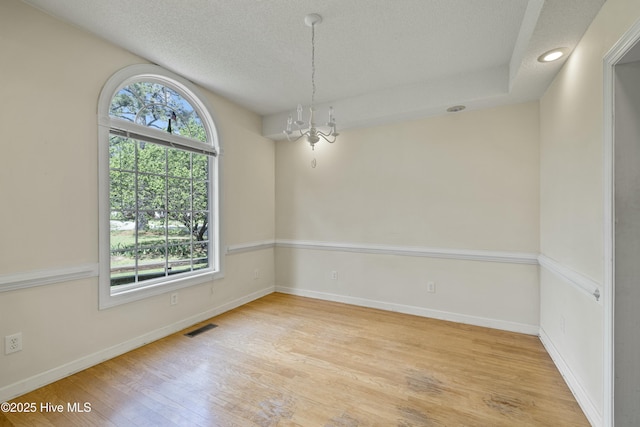 unfurnished room with baseboards, an inviting chandelier, a textured ceiling, visible vents, and wood finished floors