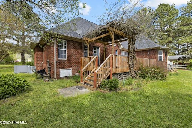 back of property featuring roof with shingles, brick siding, a wooden deck, and a lawn