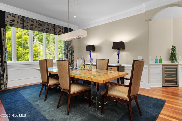 dining space featuring arched walkways, bar, light wood-style floors, crown molding, and beverage cooler