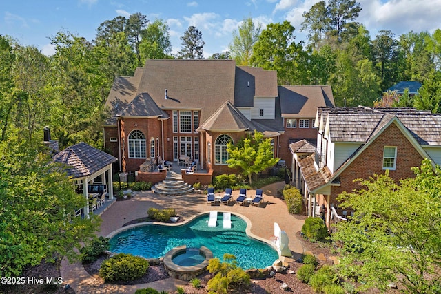rear view of house with a patio, brick siding, a pool with connected hot tub, and a gazebo