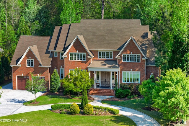 view of front of house with a front lawn, driveway, a shingled roof, a garage, and brick siding