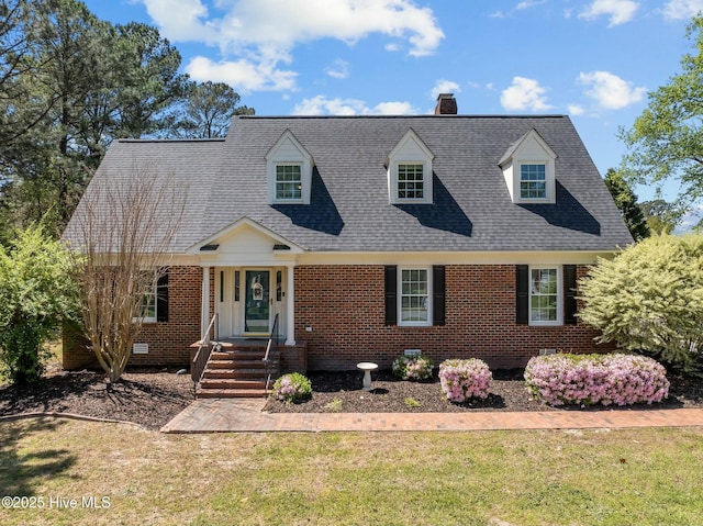 cape cod house with a chimney, a shingled roof, a front lawn, and brick siding