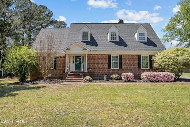 new england style home featuring a front yard, brick siding, a chimney, and a shingled roof