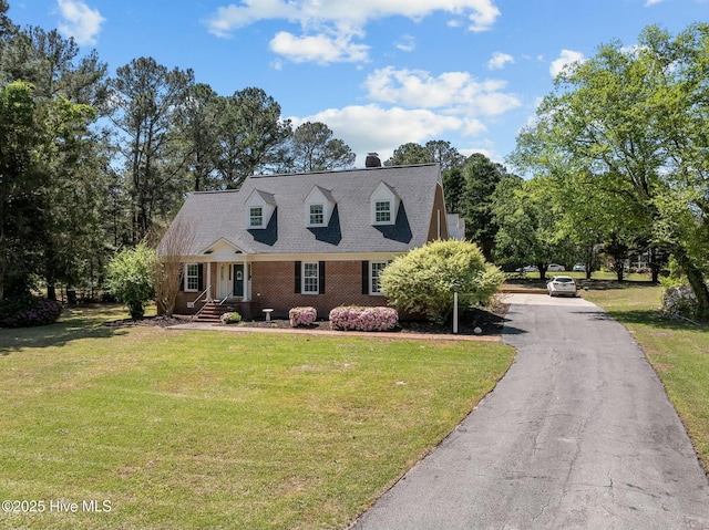 cape cod house with brick siding, a front lawn, a shingled roof, and a chimney