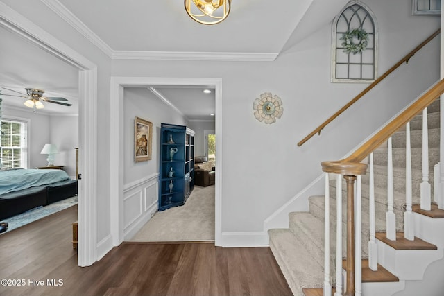 entryway featuring a ceiling fan, dark wood-style flooring, ornamental molding, and stairs